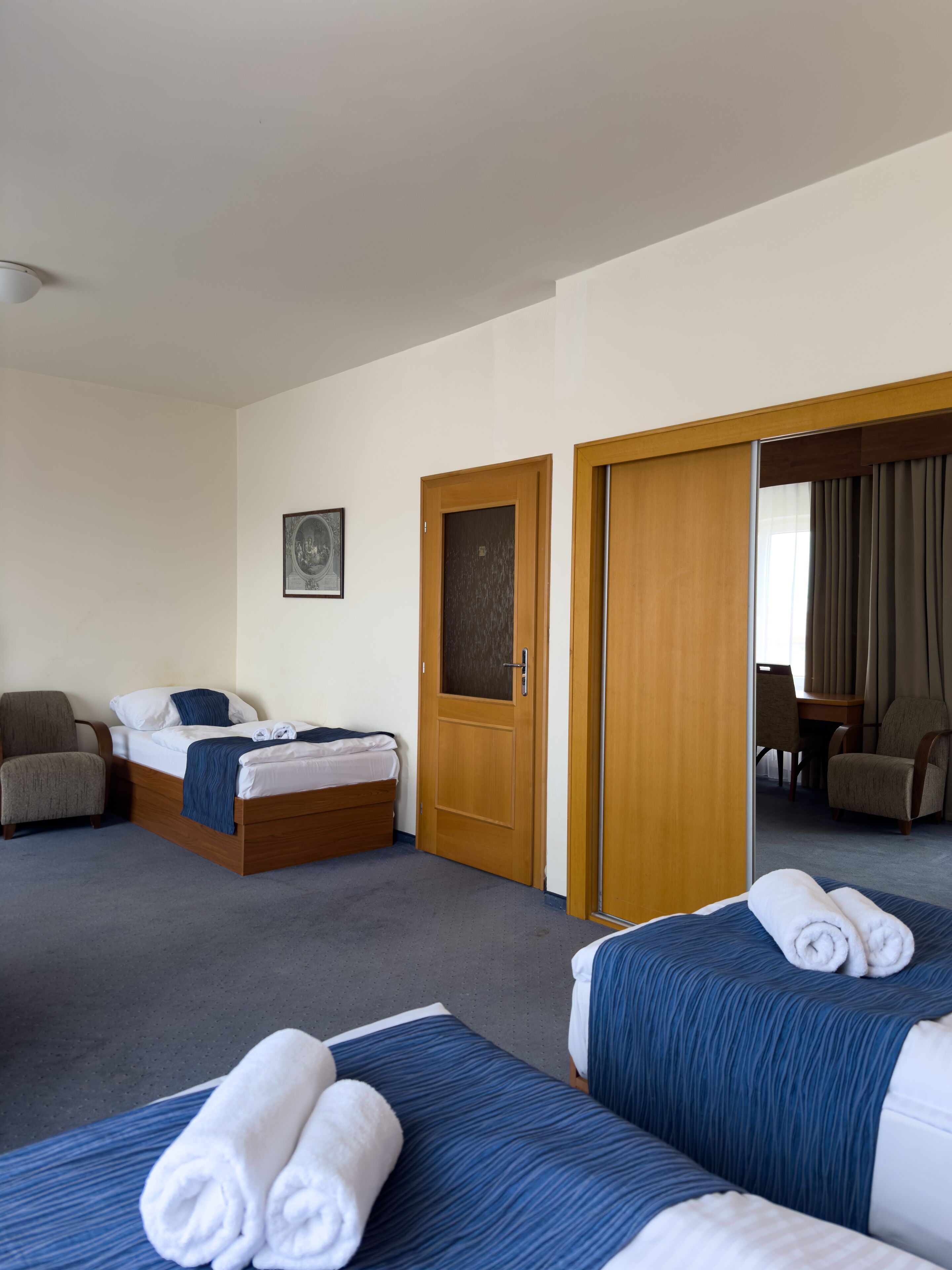 Een hotelkamer met twee bedden, een stoel, een bureau en een deur die naar een andere kamer leidt.