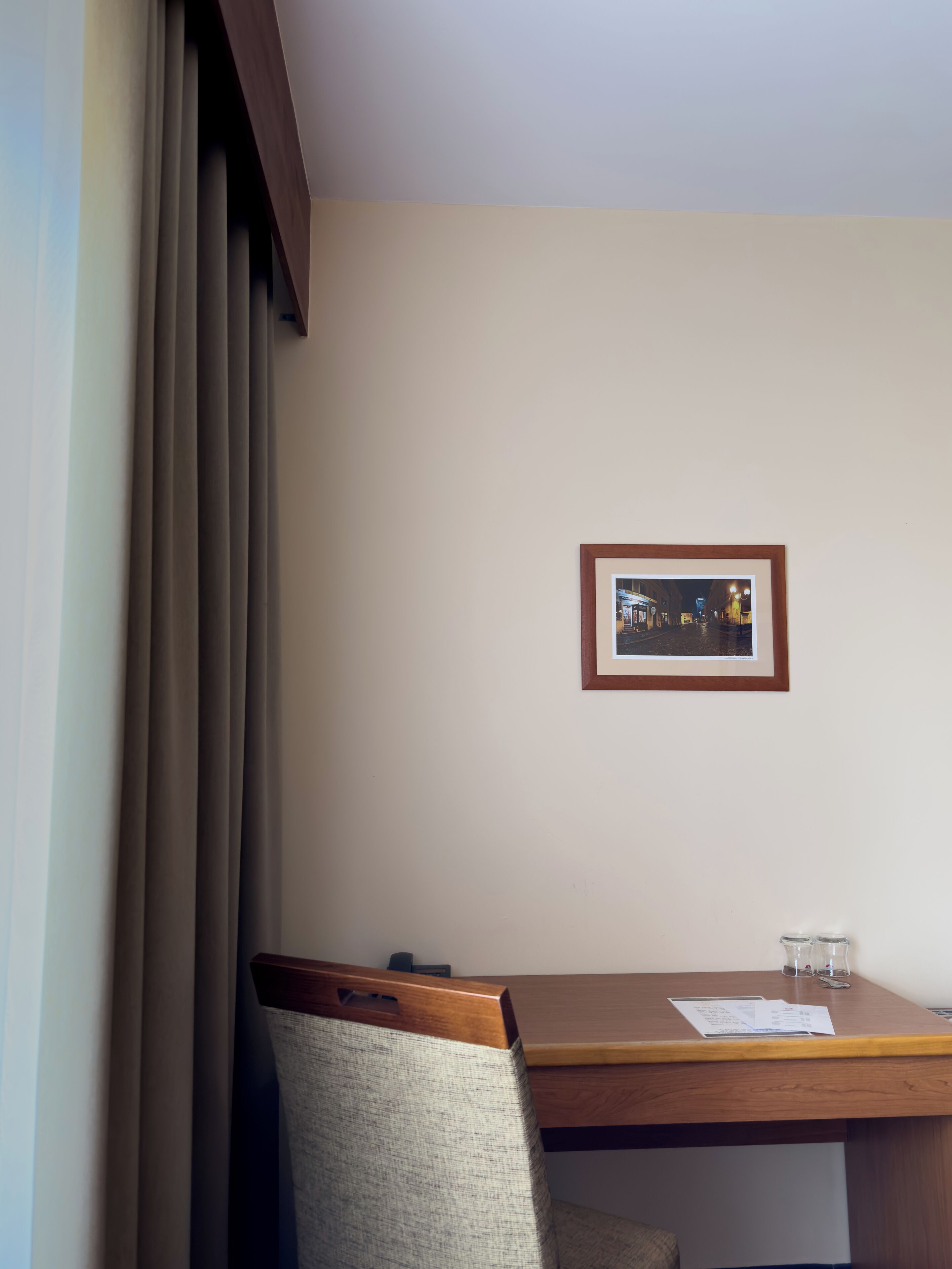 Quarto de hotel com escrivaninha de madeira, quadro pendurado na parede e uma cadeira.