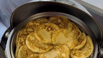 A round, stainless steel appliance with a dome-shaped lid, containing several pancakes stacked inside.