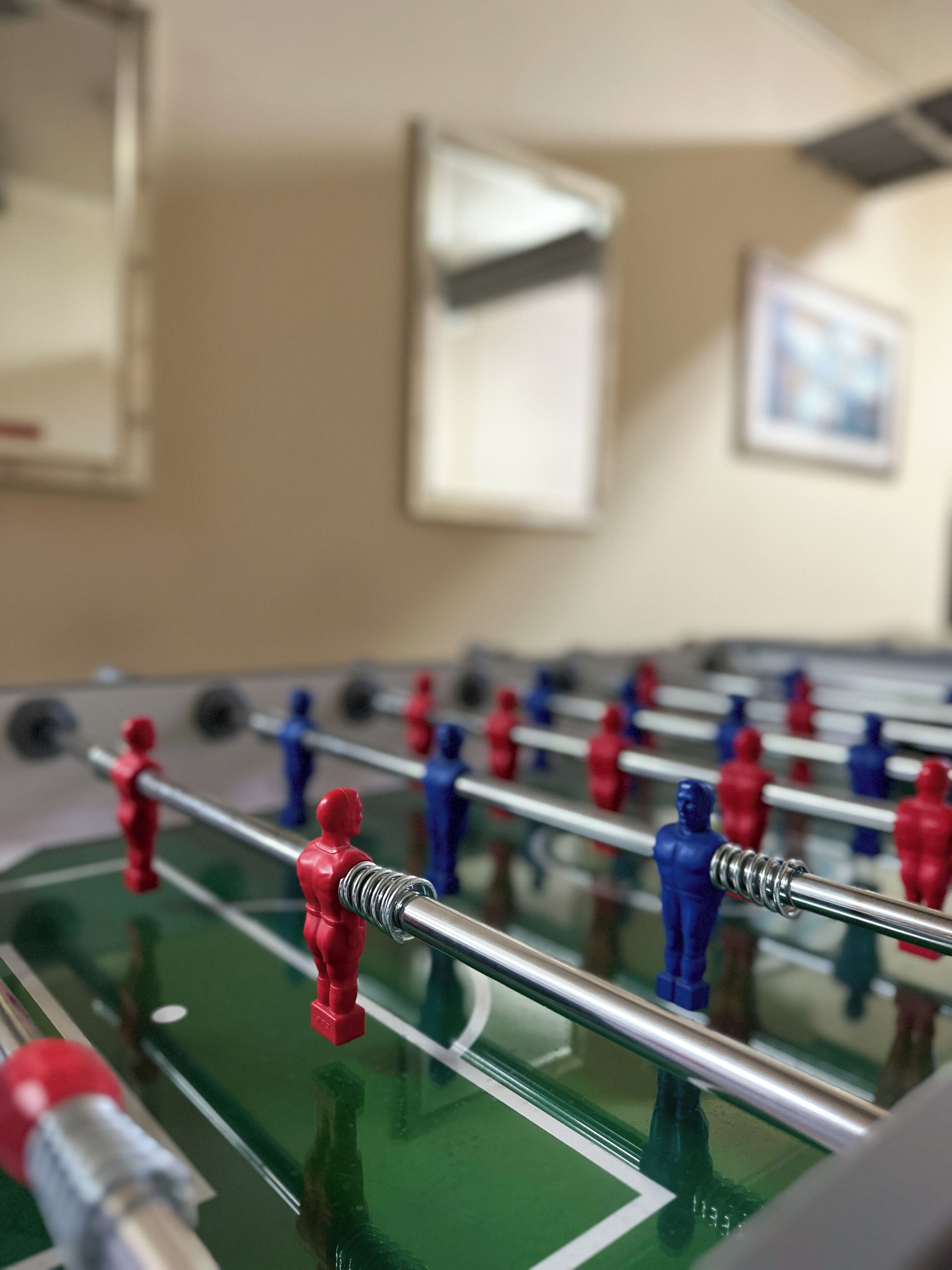 Een tafelvoetbaltafel met rode en blauwe figuurtjes, voor een muur met ingelijste foto's.