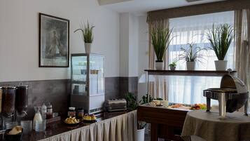 Una barra de desayuno con una cafetera, un tostador y una variedad de alimentos. Hay plantas en macetas y un cuadro en la pared.