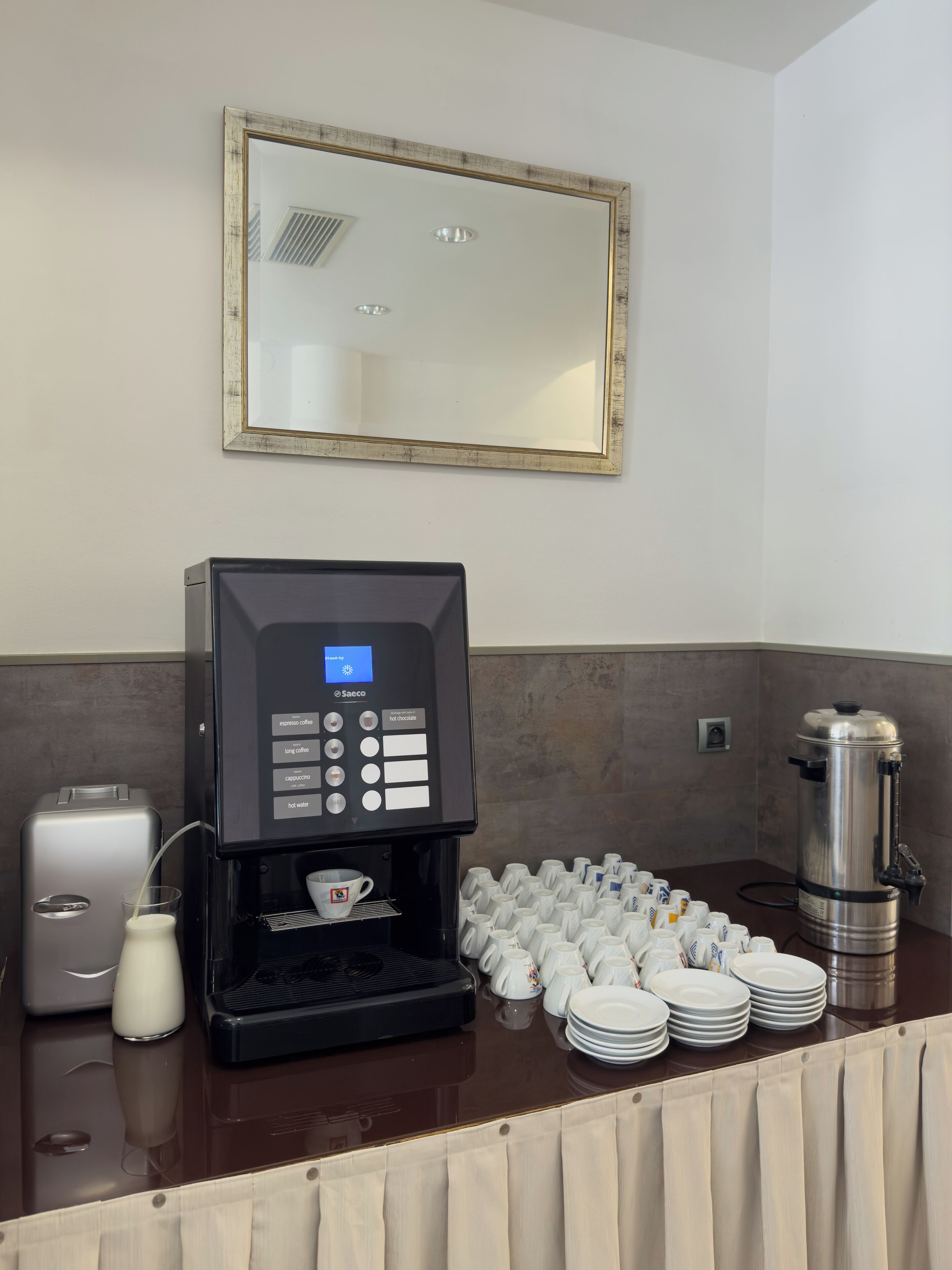 Uma estação de café com máquina de café, espumador de leite e uma pilha de copos descartáveis.