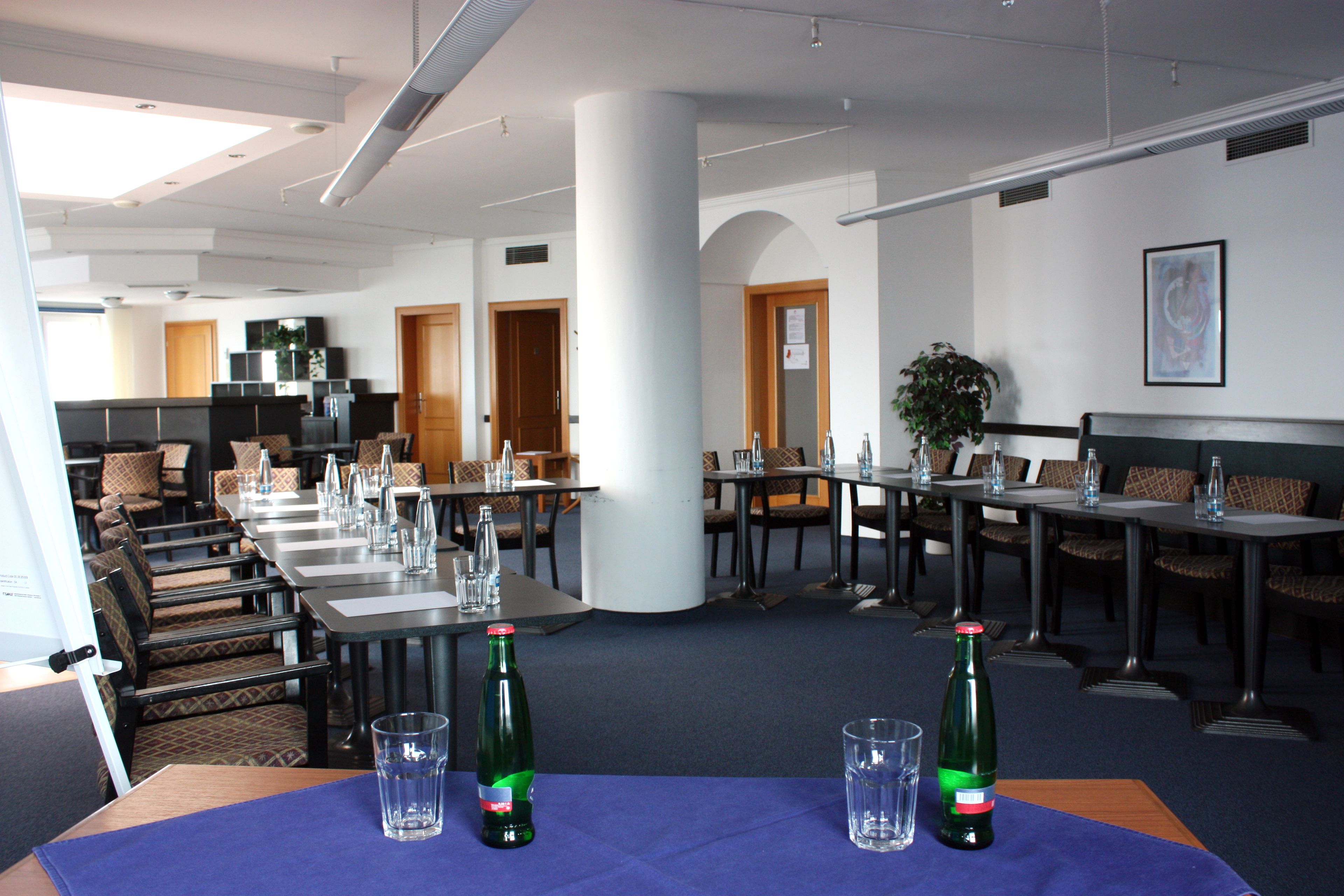 Un salón de conferencias con mesas dispuestas para reuniones, un pilar grande y una planta en maceta.