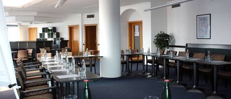 Un salón de conferencias con mesas dispuestas para reuniones, un pilar grande y una planta en maceta.
