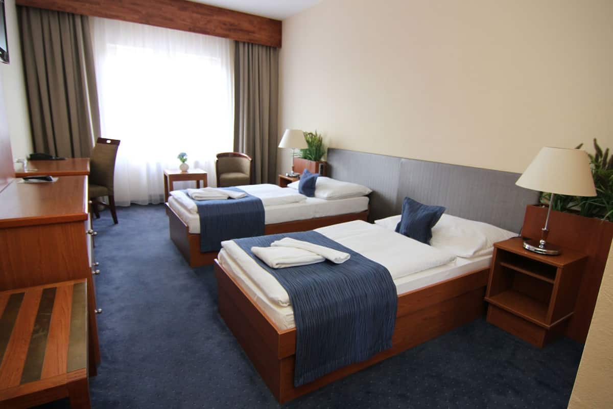 Ein Hotelzimmer mit zwei Betten, einem Schreibtisch, einem Stuhl, einer Lampe und einem Vorhangfenster.