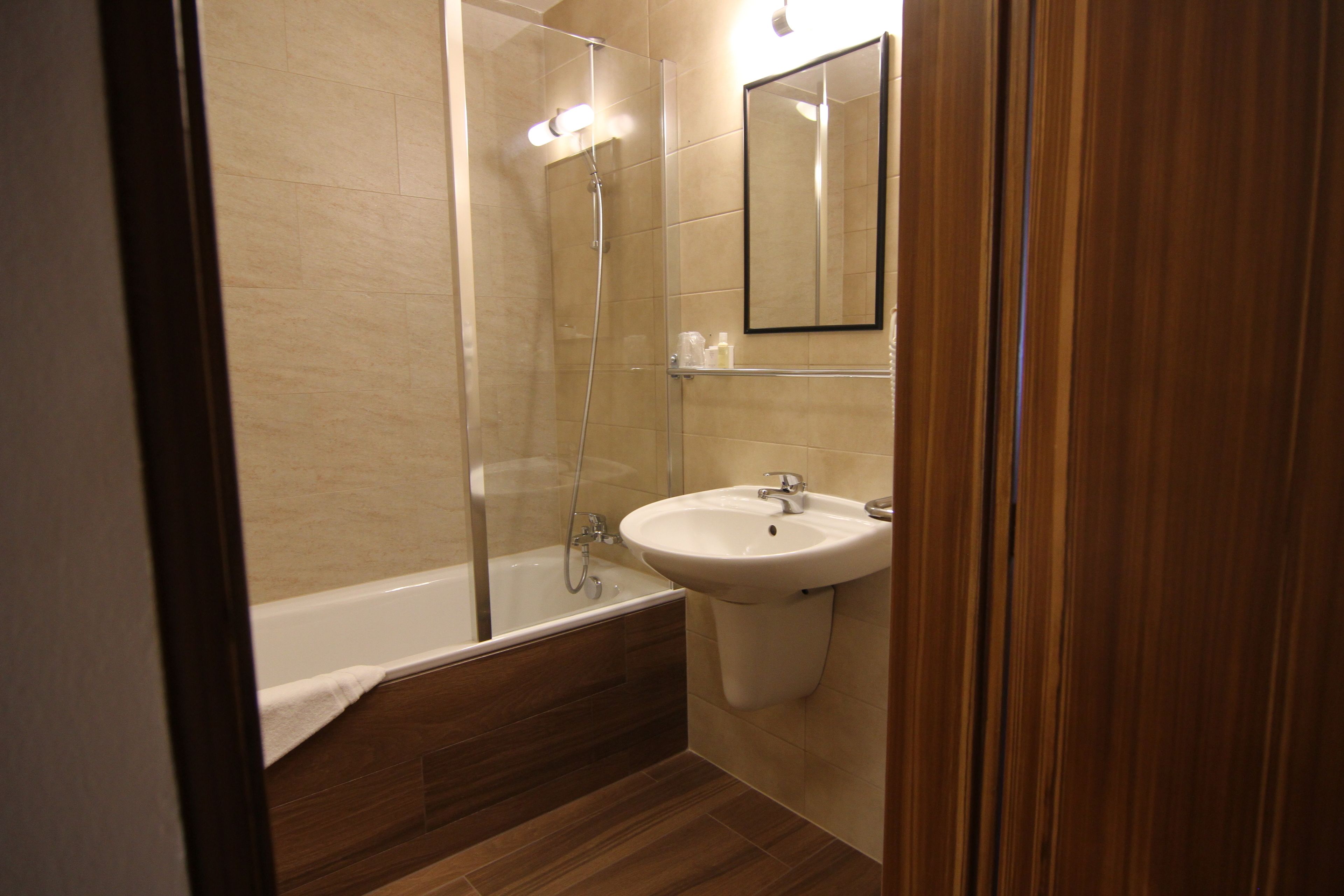 A modern bathroom with a glass-enclosed shower, a white sink, and a wooden floor.