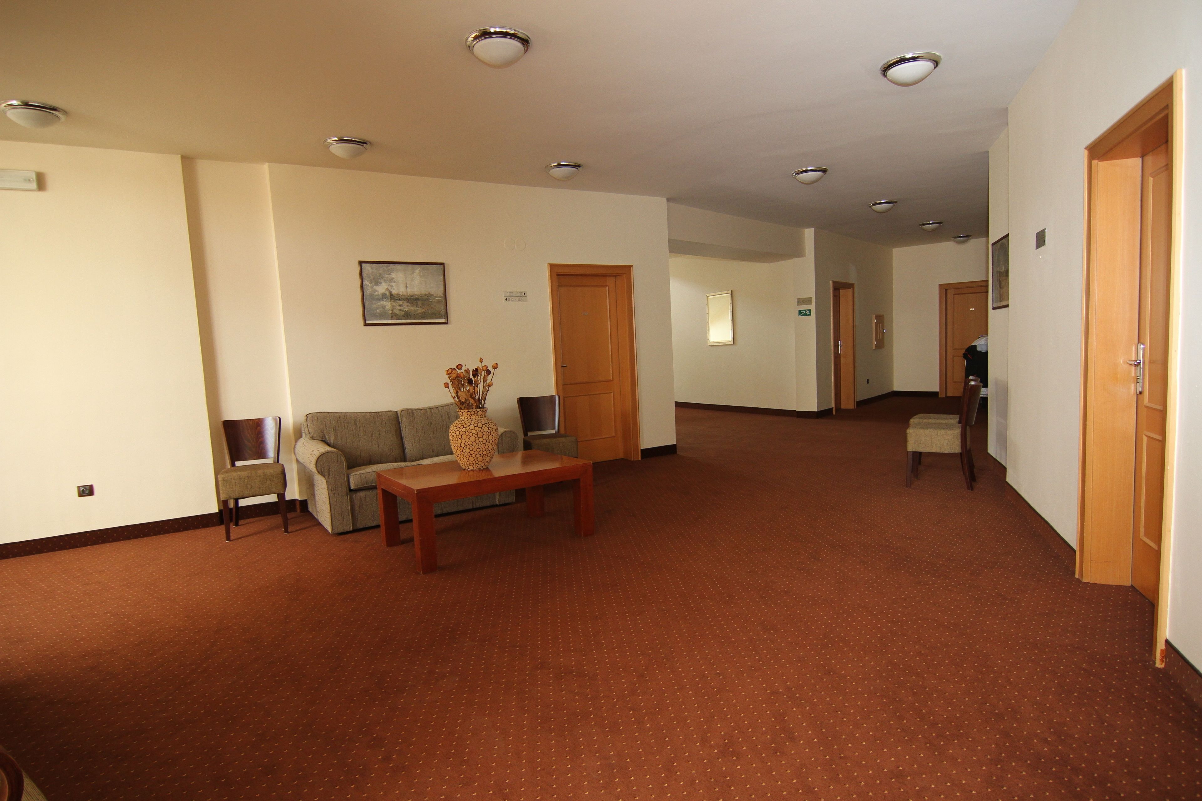 A spacious hallway with a brown carpet, a wooden table, two sofas, and a vase of dried flowers.