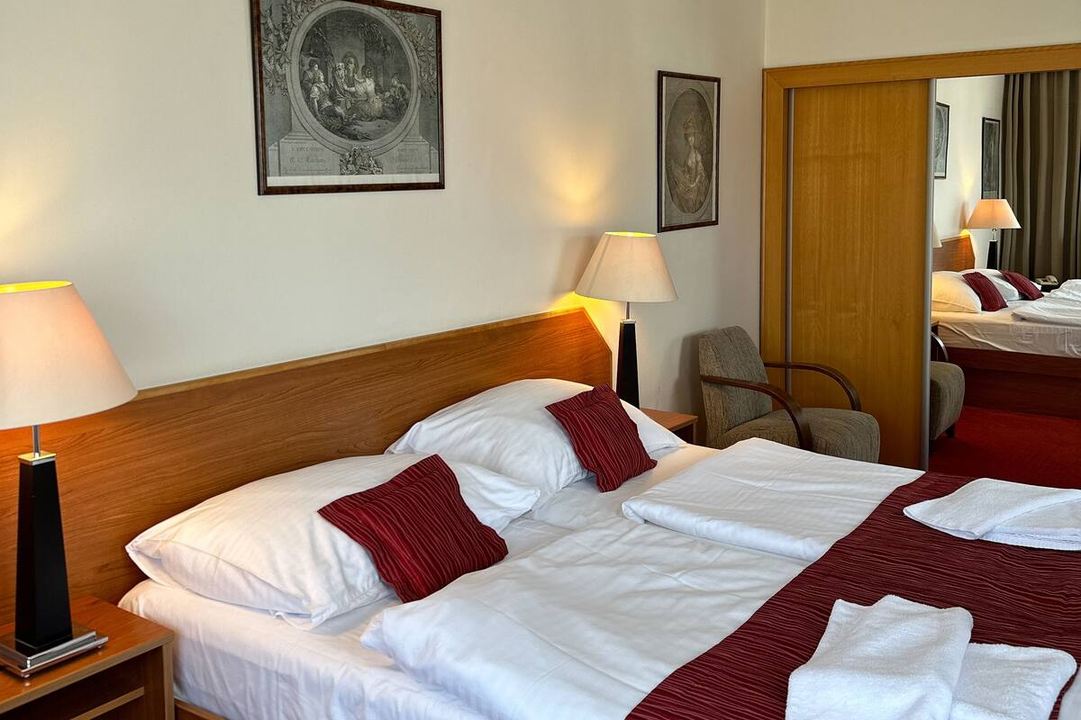 Ein Hotelzimmer mit einem großen Bett, zwei Nachttischen, einem Holzkopfstück und zwei gerahmten Kunstwerken an der Wand.