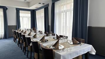 Mesa de jantar comprida posta para uma refeição formal num quarto de hotel com janelas amplas e cortinas.
