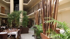 A spacious indoor dining area with multiple tables and chairs, surrounded by tall bamboo plants and potted greenery. - Hotel Theresia Kolín (Kolin)