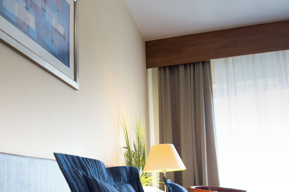 Ein Hotelzimmer mit zwei Betten, einem Gemälde an der Wand, einer Lampe und einem Fenster mit Vorhängen.