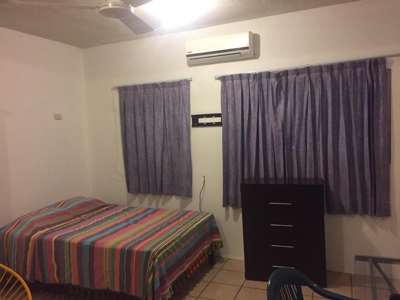 Una habitación pequeña con cama, cómoda y aire acondicionado.