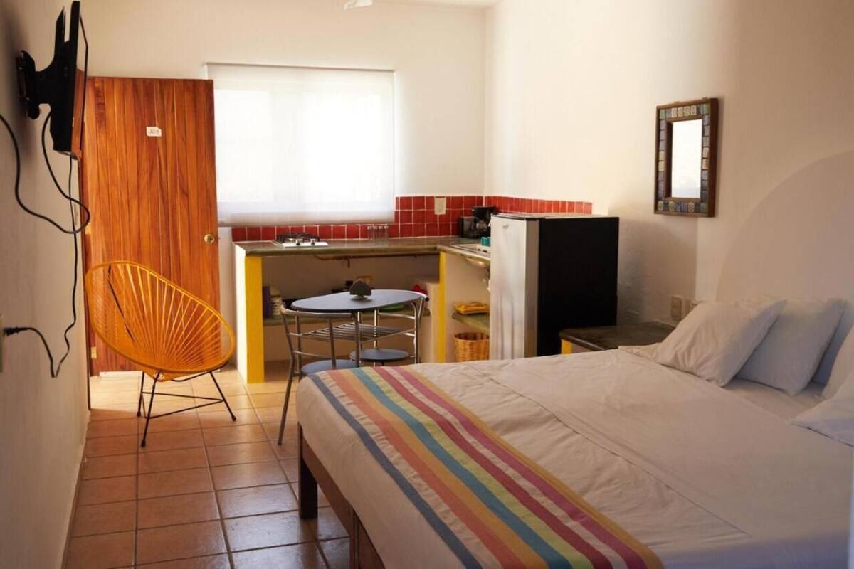 Una habitación de hotel compacta con una cama, un pequeño rincón americano, una mesa de comedor y una silla.