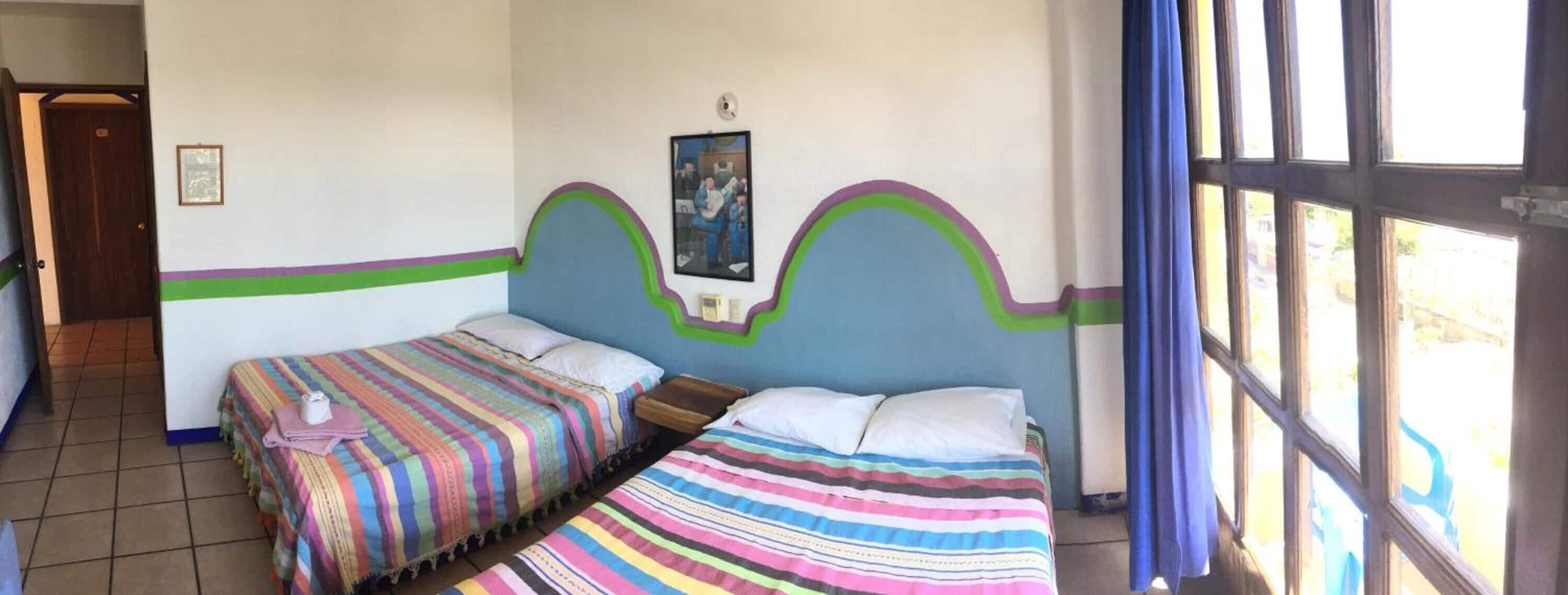 A room with two beds, a window with curtains, and a door.