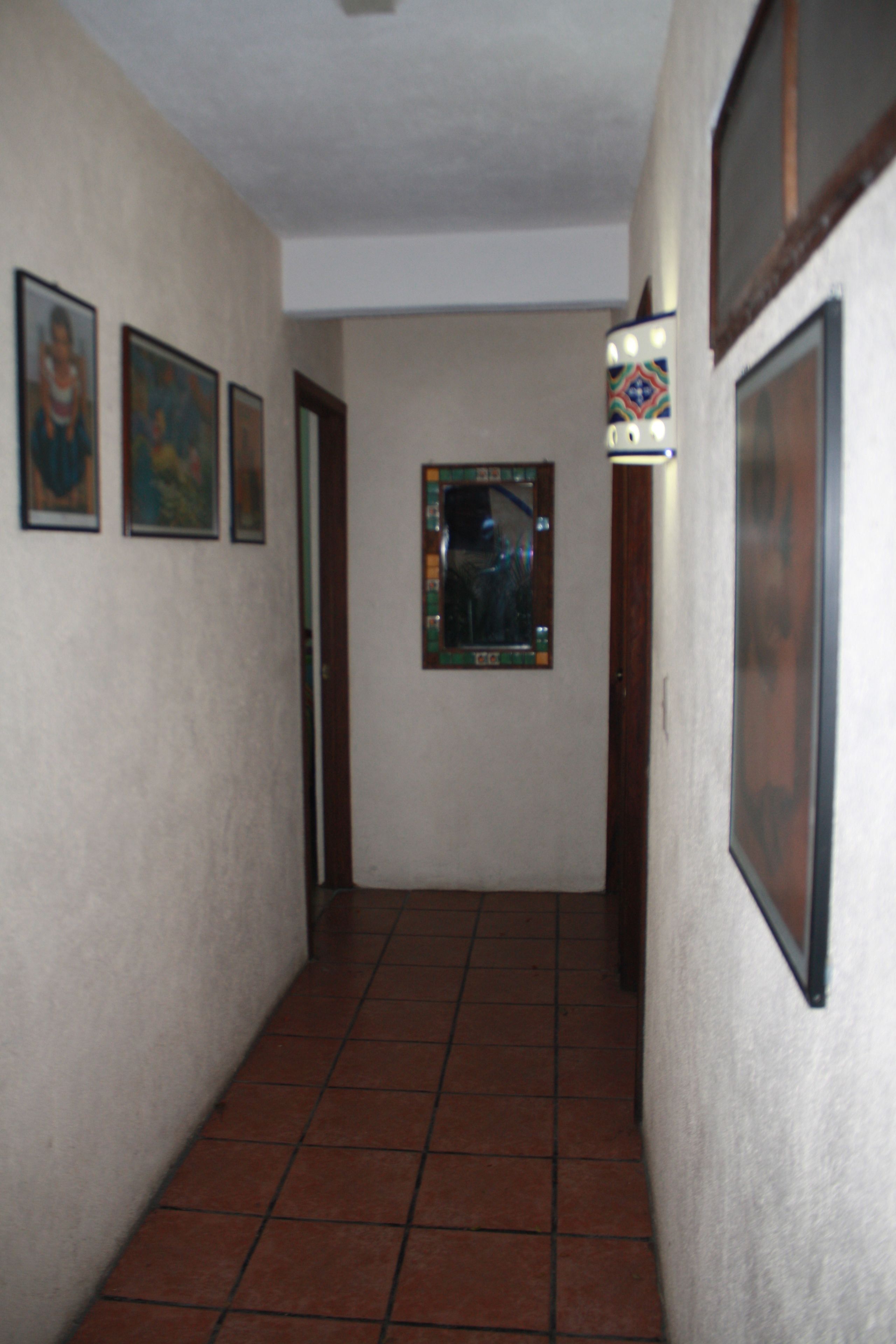 A hallway with tiled flooring, framed pictures on the walls, and a door at the end.