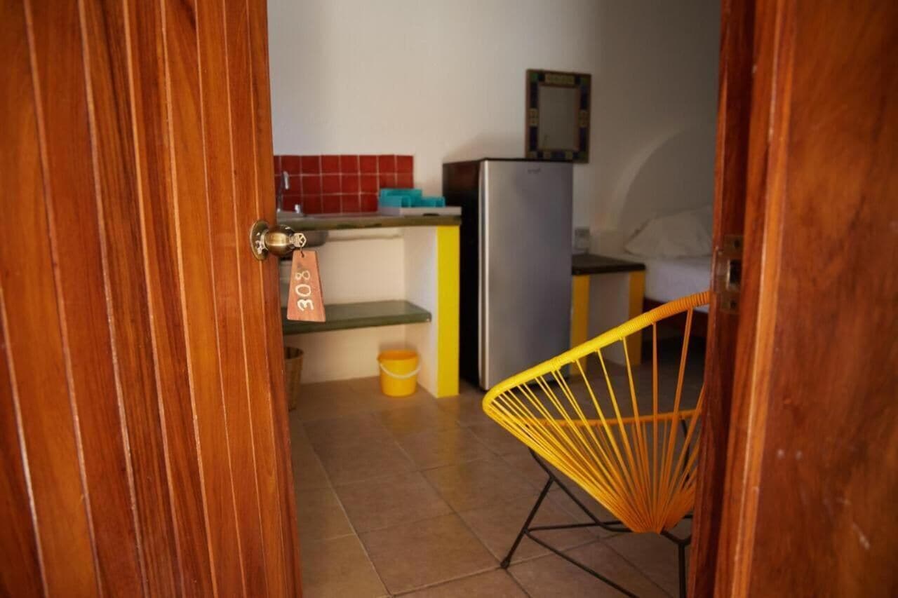 A compact kitchen with a refrigerator, a yellow chair, and a small table.
