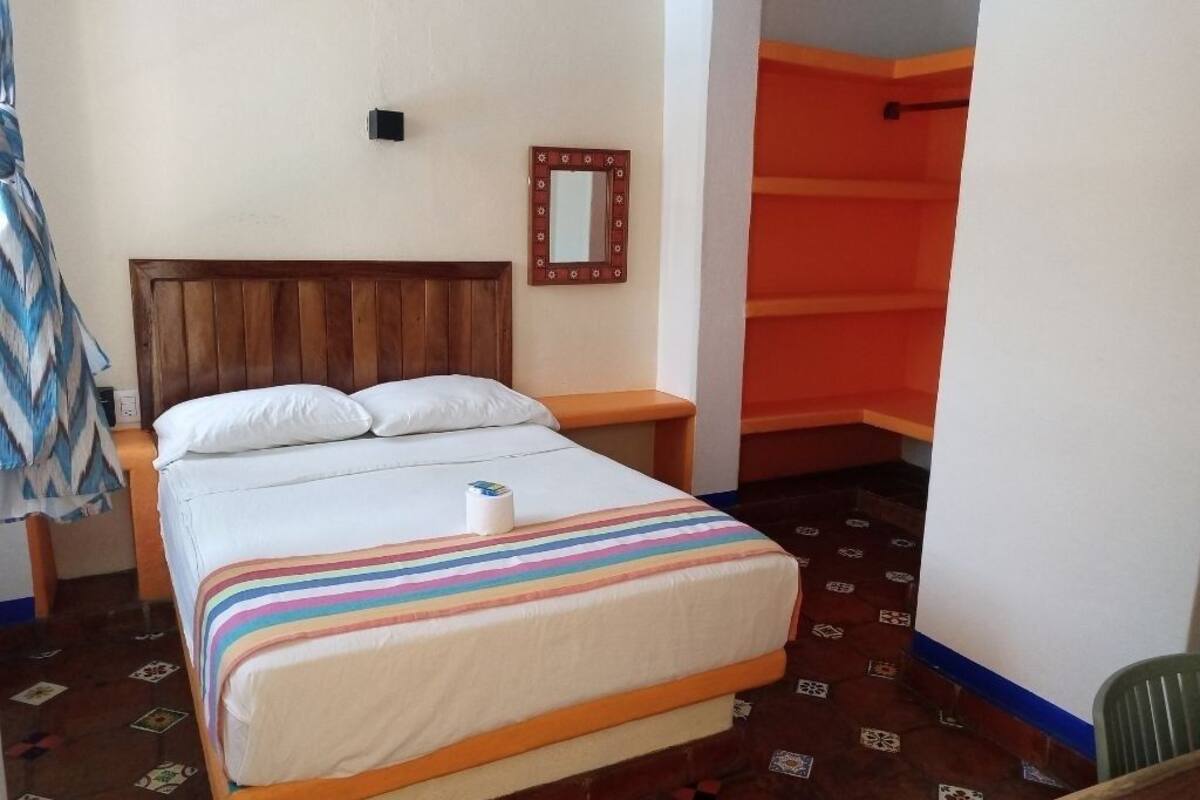 Una habitación de hotel con una cama de madera, una colcha a rayas, una mesita de noche pequeña y un espejo en la pared.