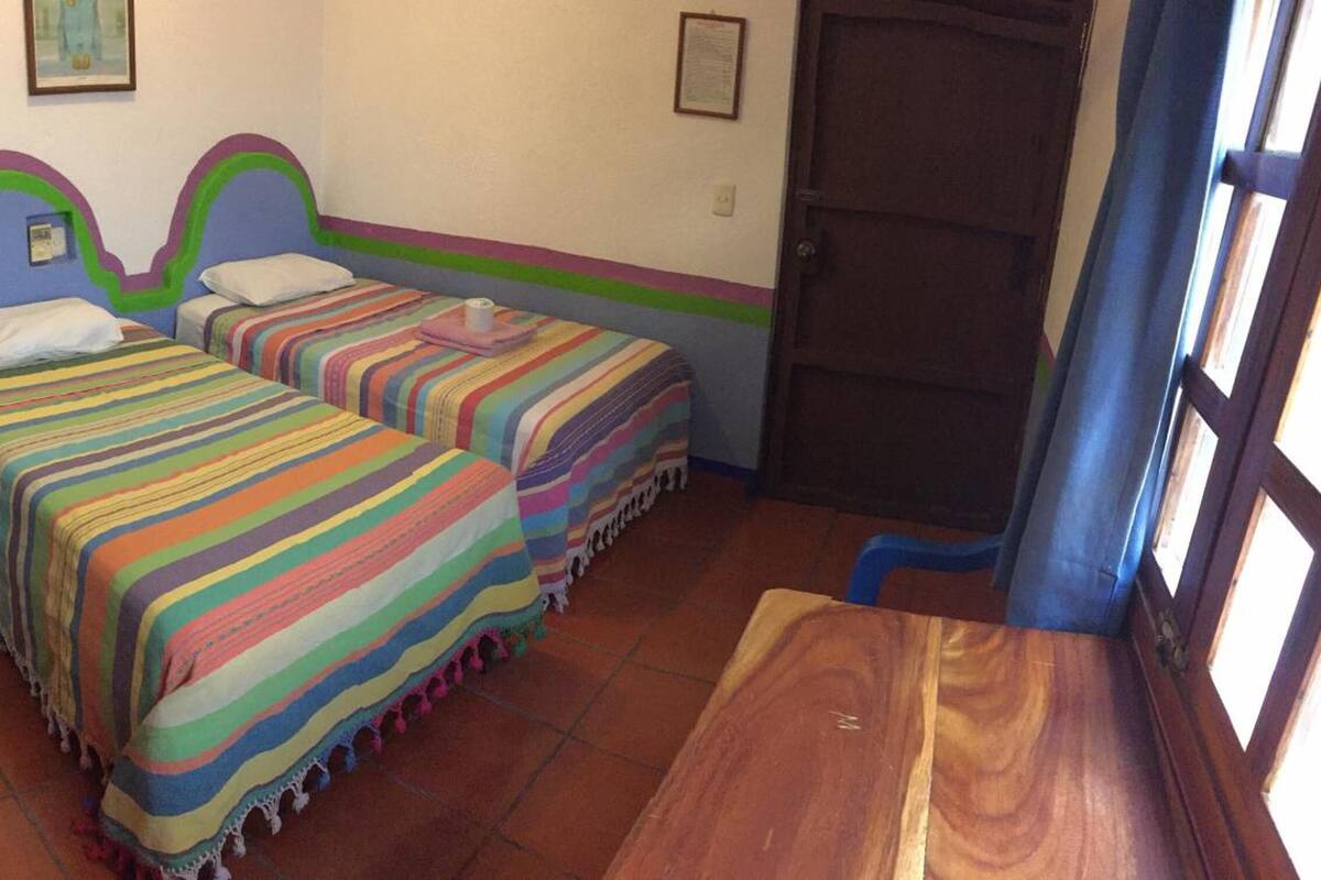 Una habitación con dos camas, una mesa de madera y una puerta.