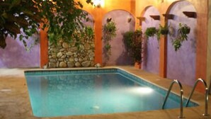 A rectangular indoor swimming pool with a stone wall and arches in the background. - Pargo's Hotel (Puerto Escondido)