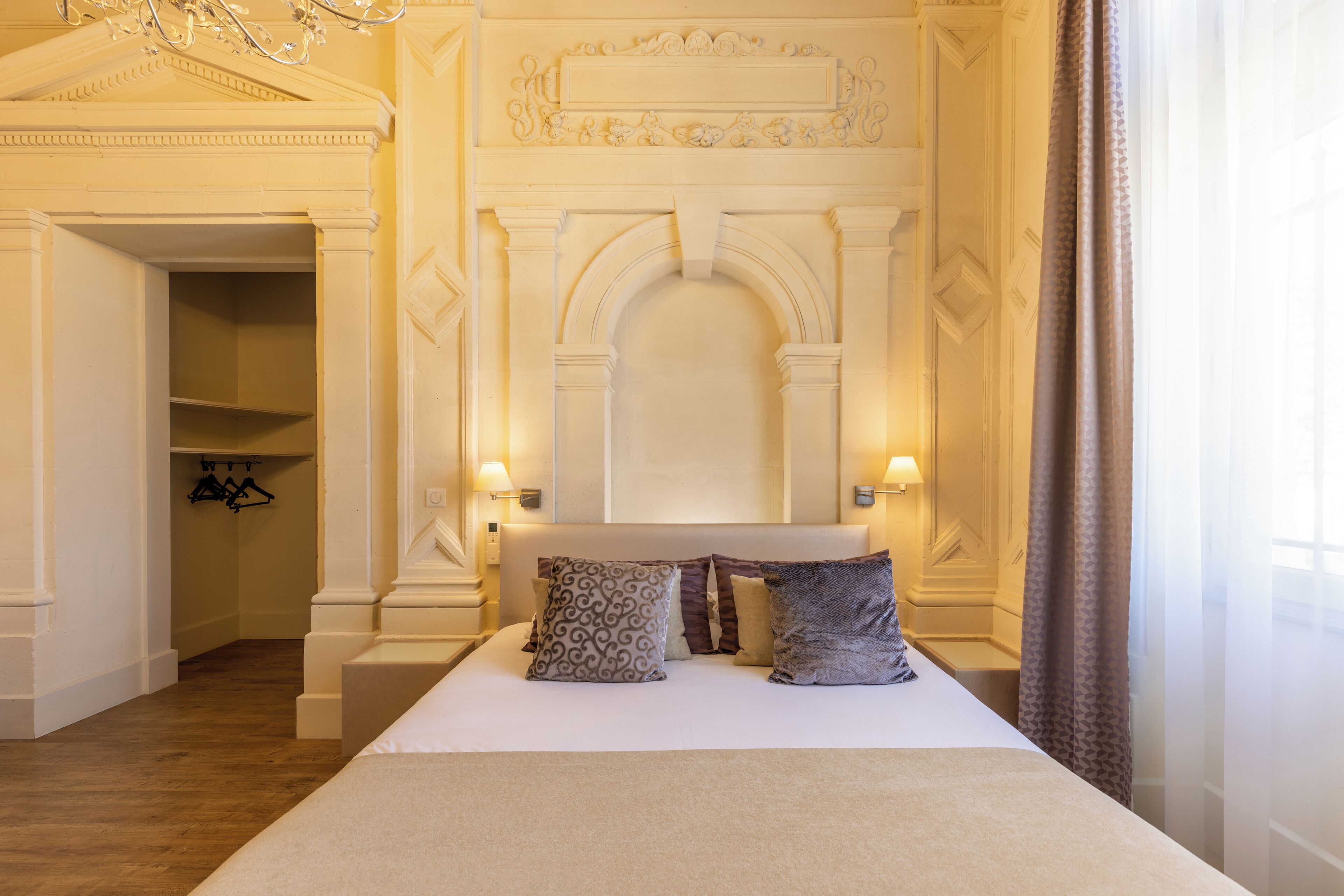 A hotel room with a large bed, a chandelier, and a view of the hallway.
