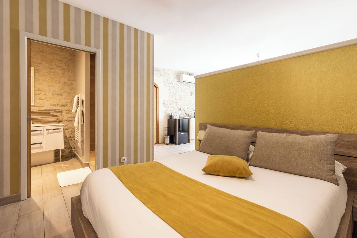 A bedroom with a bed, a wooden headboard, a yellow throw blanket, and a striped wall.
