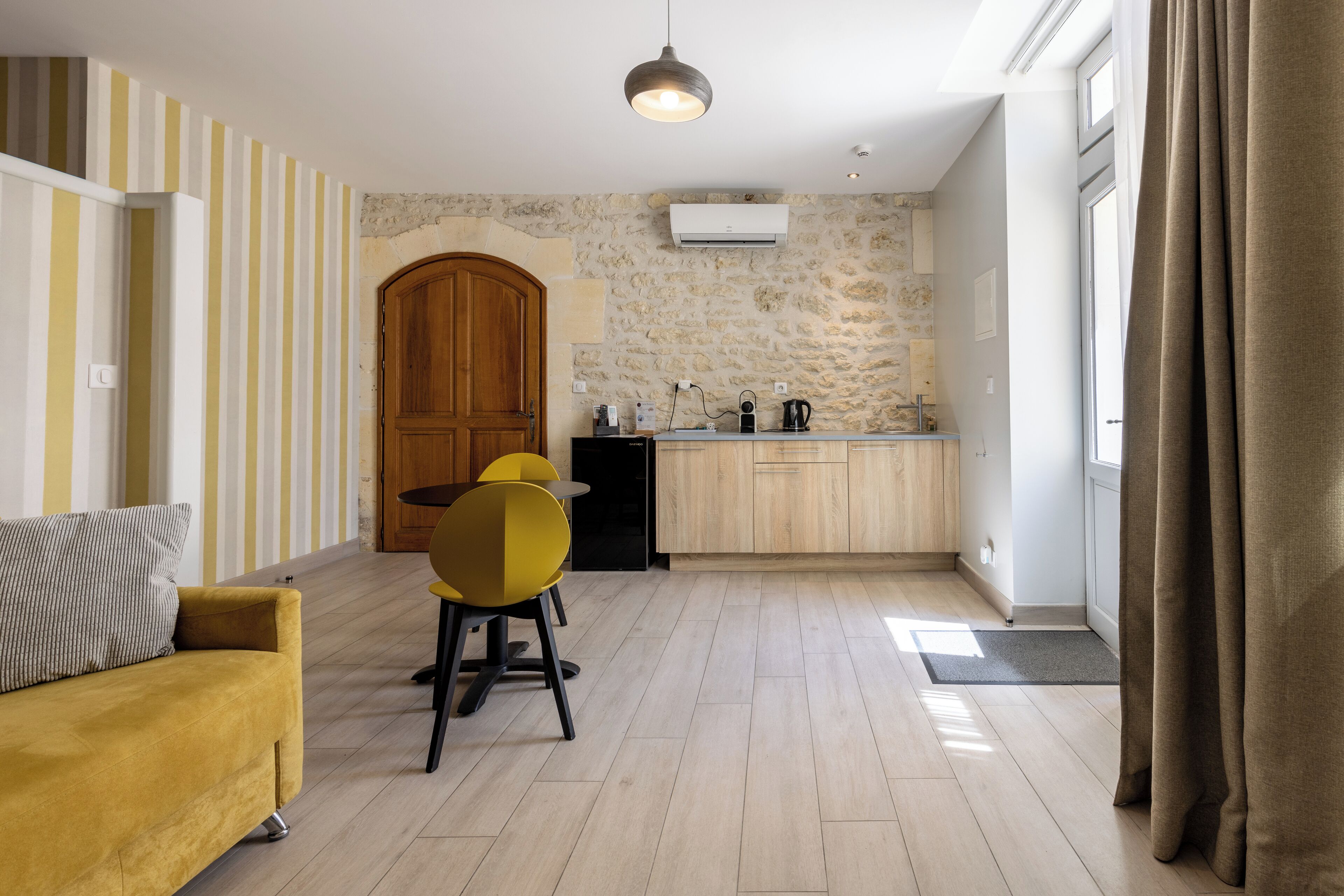 A modern kitchen with a stone wall, wooden cabinets, and a yellow chair.