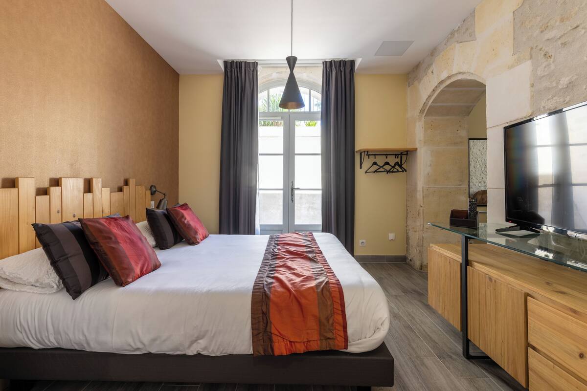 A bedroom with a bed, a desk, a TV, and a window with curtains.