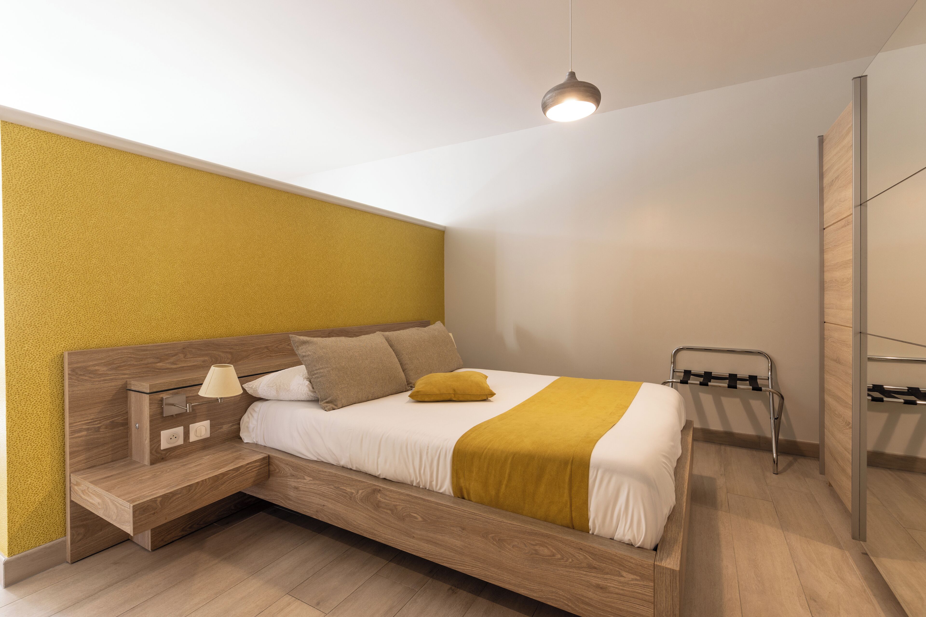 A modern bedroom with a wooden bed, a bedside table with a lamp, and a hanging light fixture.