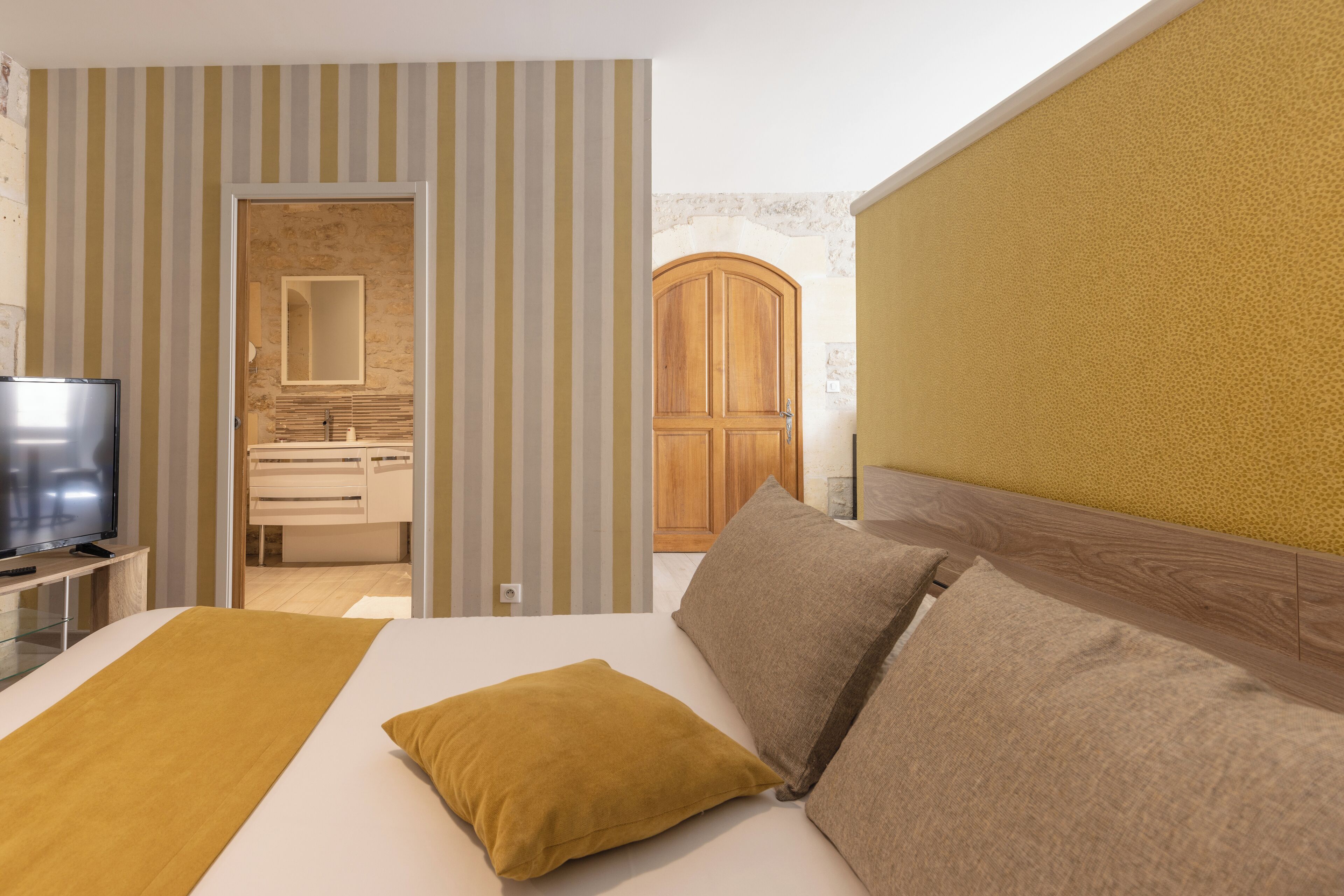 Una habitación de hotel con cama, televisor, armario de madera y baño visible a través de una puerta abierta.