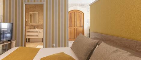 Una habitación de hotel con cama, televisor, armario de madera y baño visible a través de una puerta abierta.