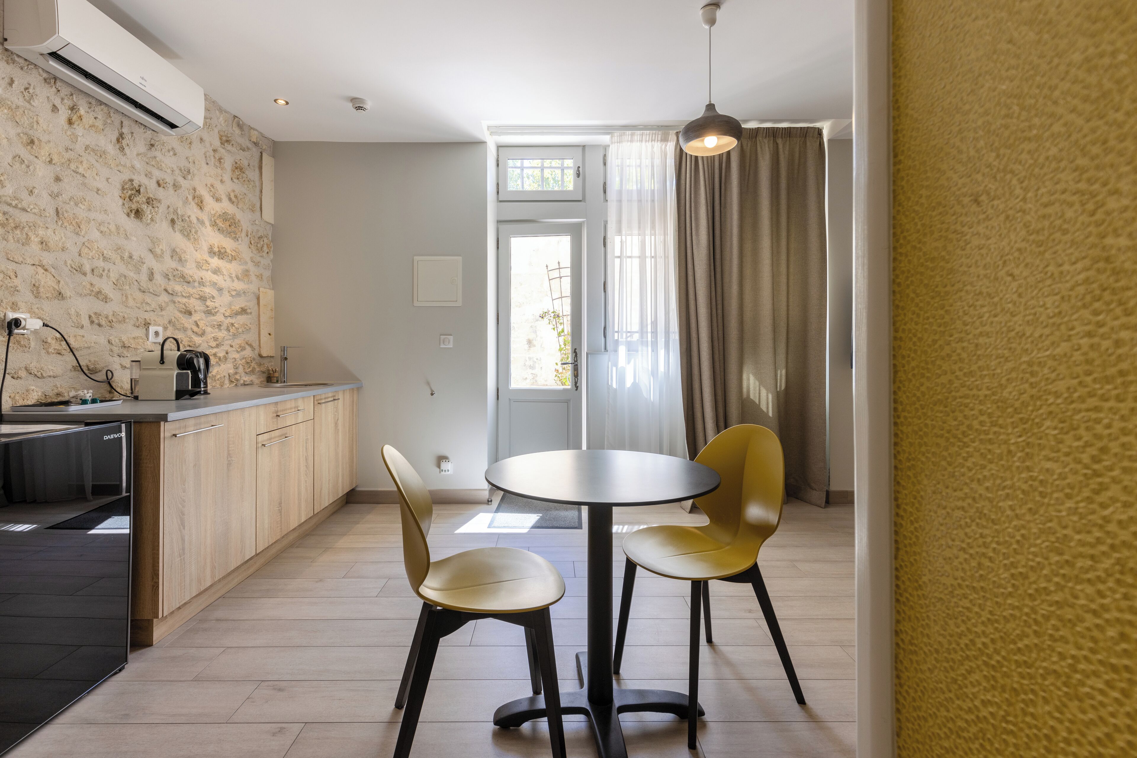 A modern kitchen with a stone wall, a built-in dishwasher, and a dining area with two yellow chairs and a round table.