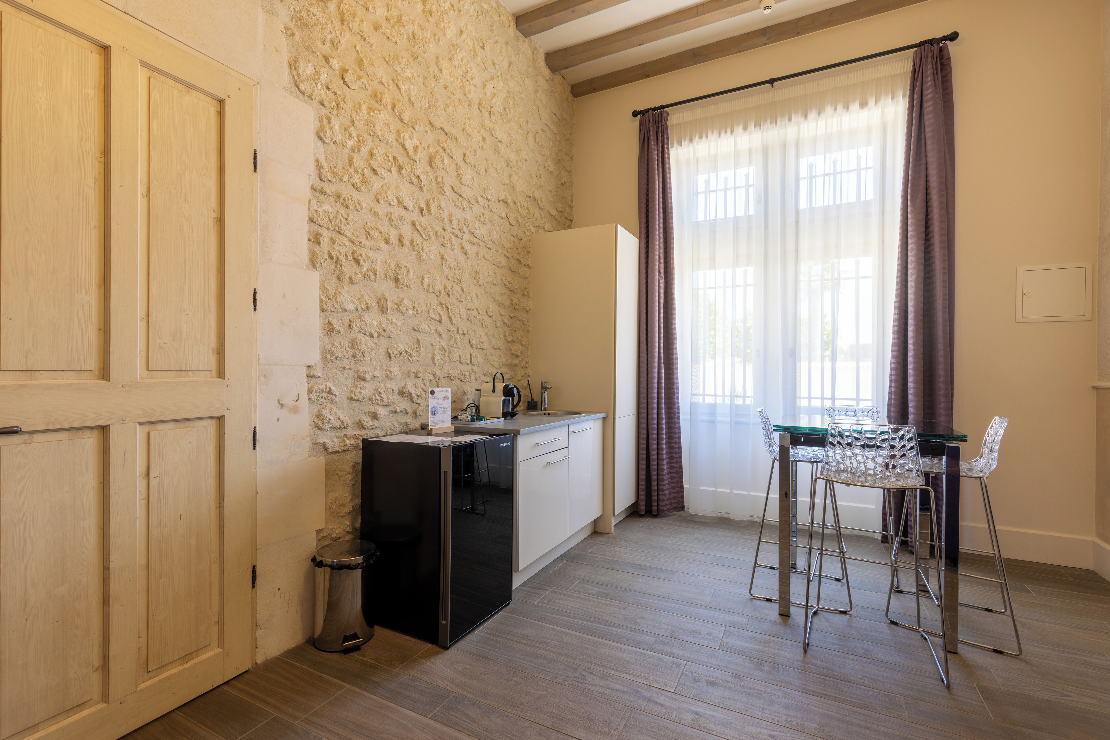 Una cocina compacta con pared de piedra, refrigerador negro, un lavamanos pequeño y una zona de bar con taburetes.