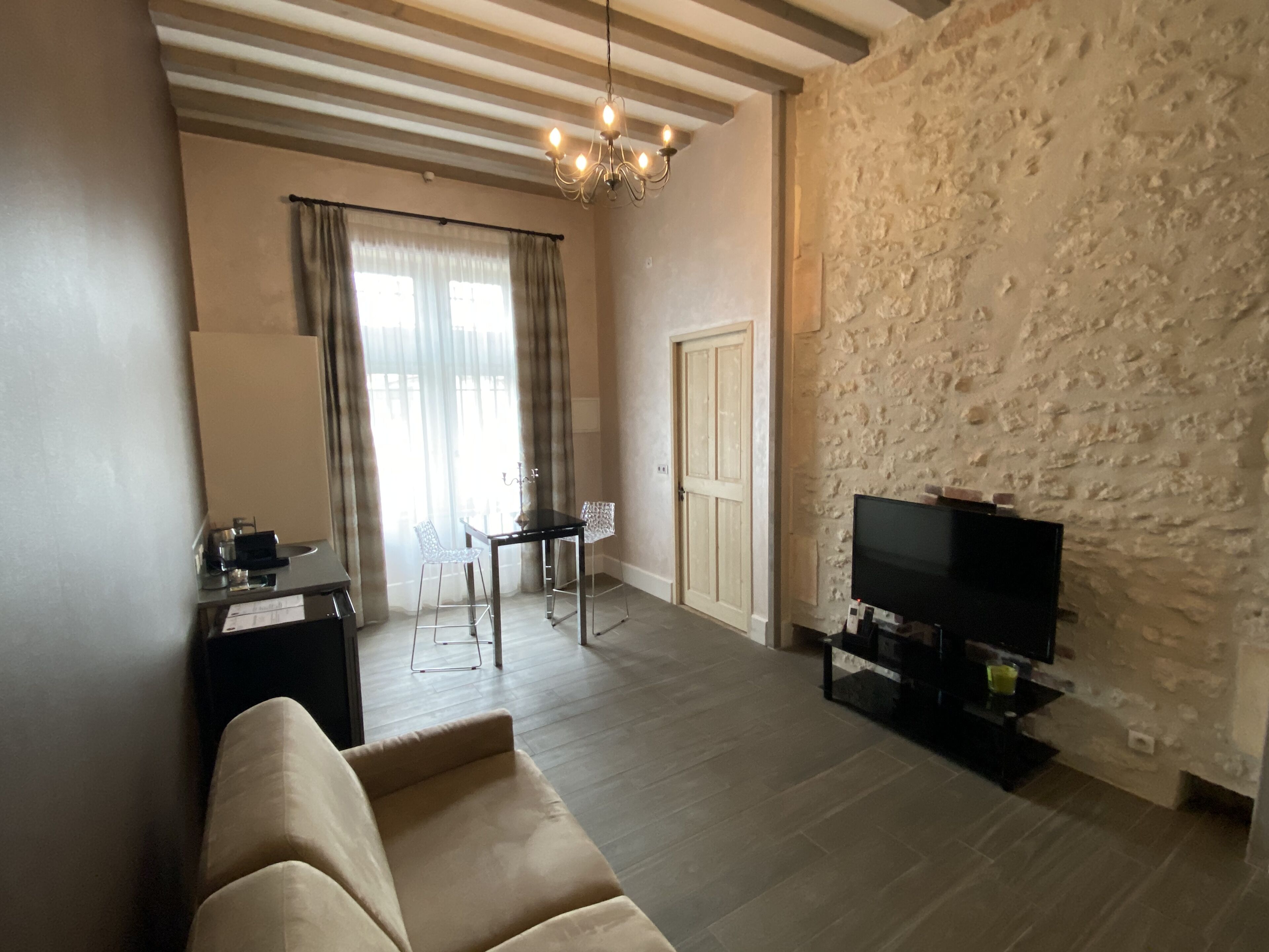 Una sala de estar con sofá, televisor, mesa de comedor con sillas, candelabro y pared de piedra.