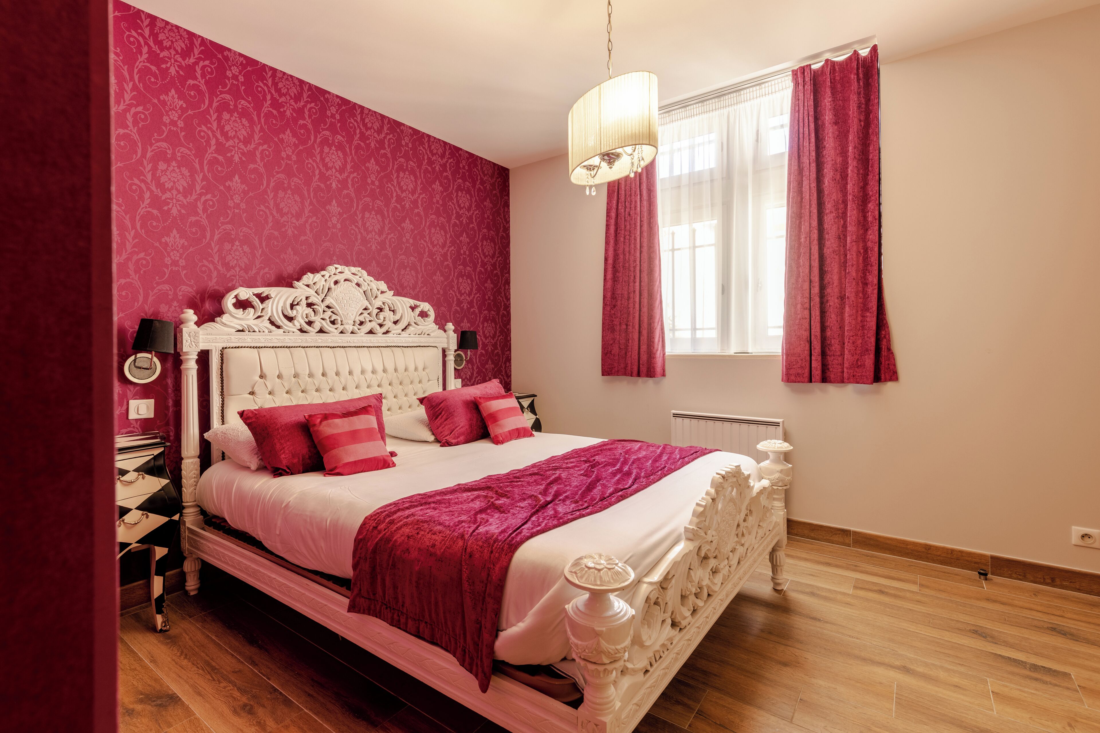 Un dormitorio con cama blanca, cortinas rojas y un candelabro.