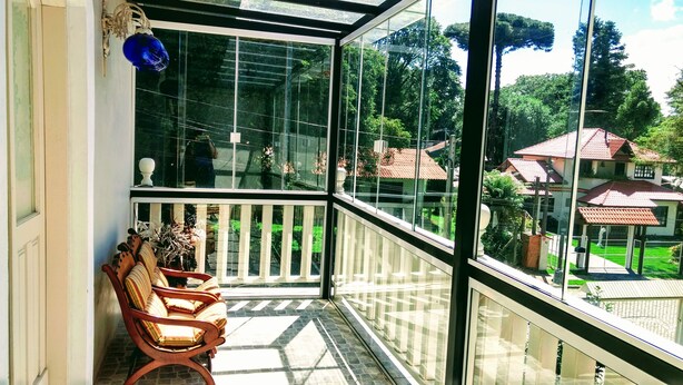 Un balcon doté d’une paroi vitrée, de chaises en bois et offrant une vue sur un quartier résidentiel.