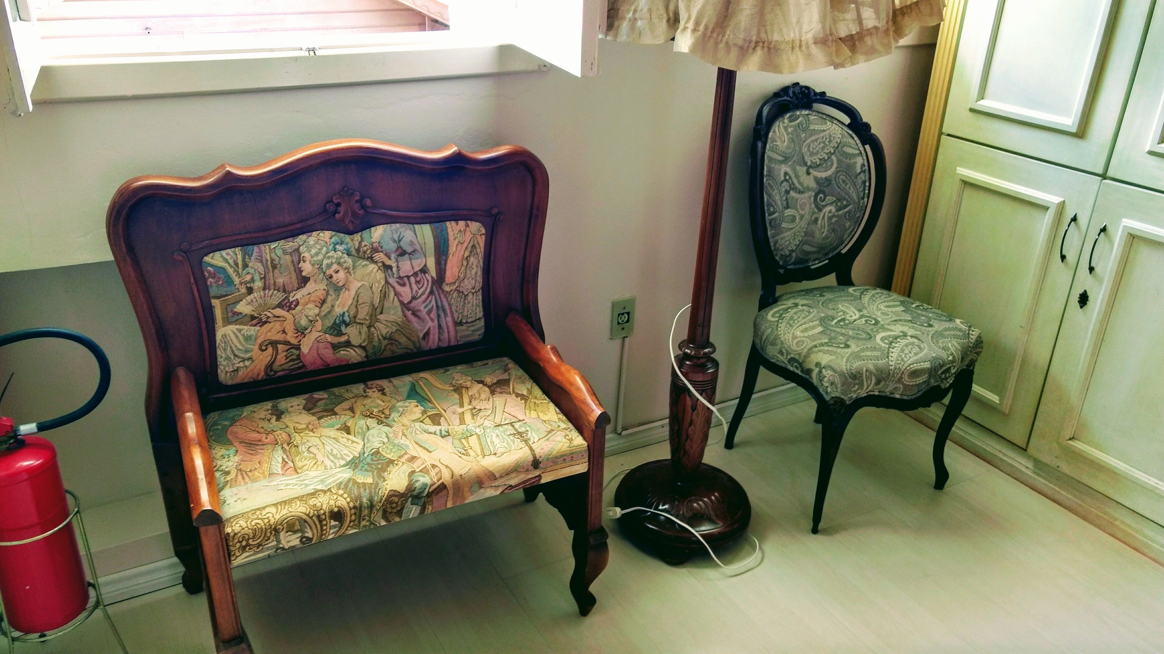 A room with a vintage-style wooden bench with a detailed backrest and a cushioned seat. A matching chair with a patterned cushion is also visible.