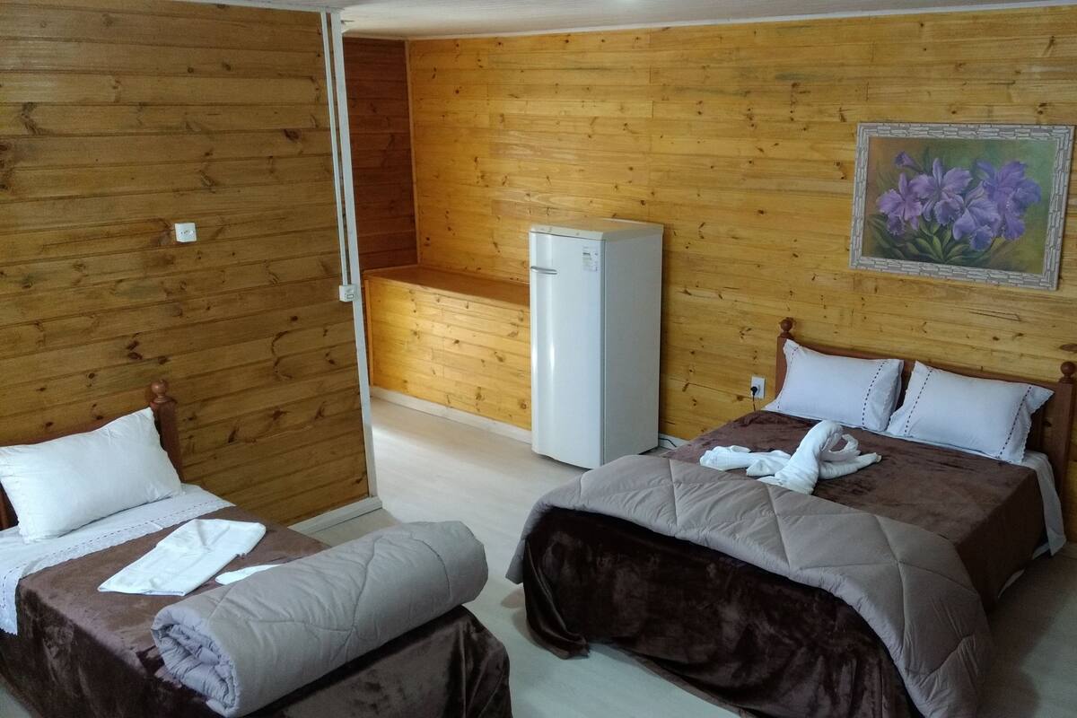 Een kamer met houten lambrisering, twee bedden, een koelkast en een bloemen schilderij aan de muur.