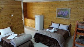 A wooden-paneled room with two beds, a refrigerator, and a painting of flowers on the wall.