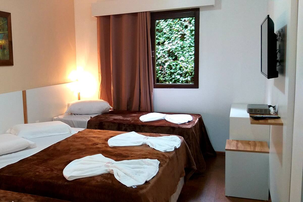 Een hotelkamer met twee bedden, een stadsgezicht op een schilderij, een raam met gordijnen en een televisie aan de muur.