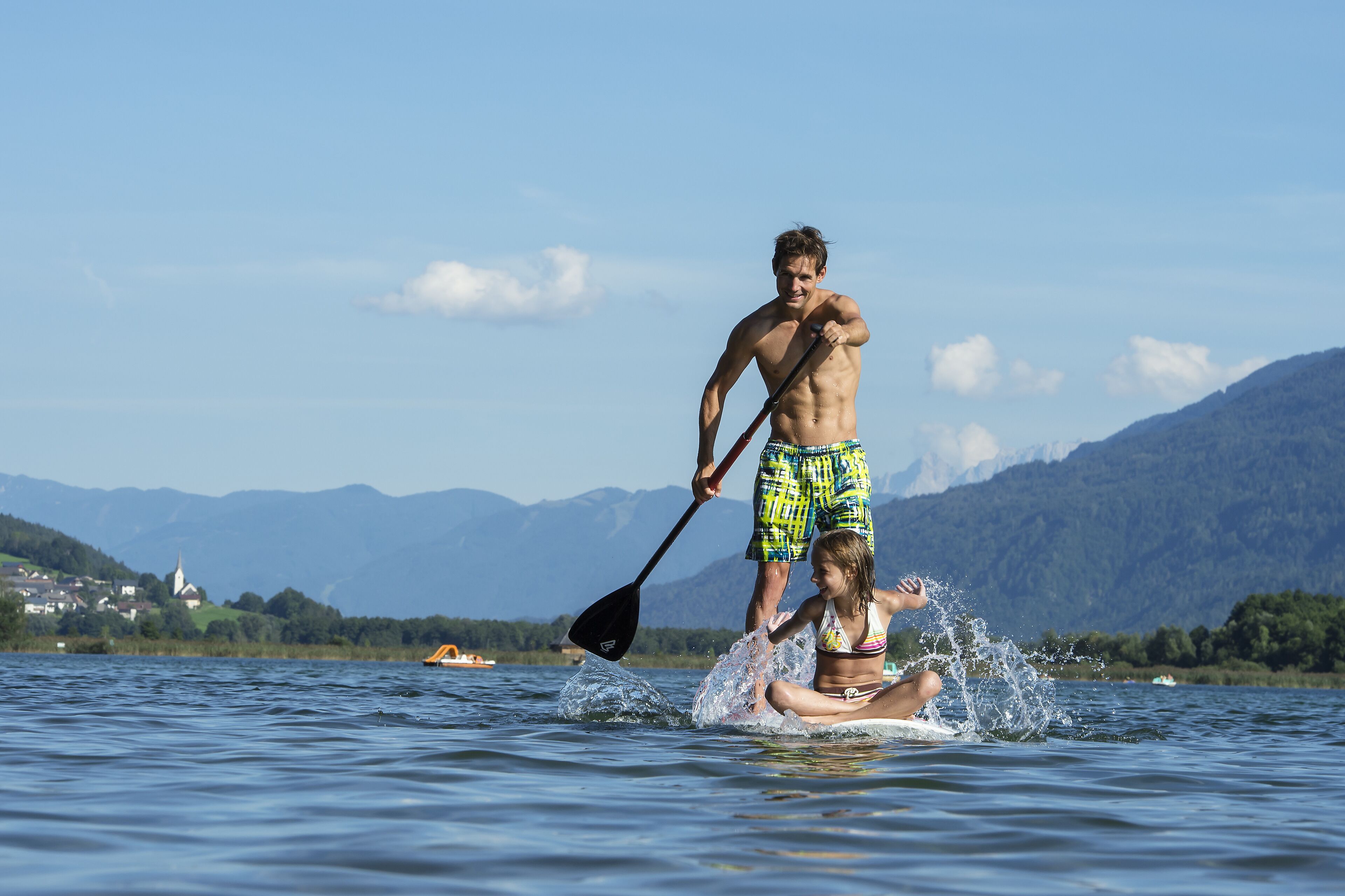 Un uomo e una donna su una tavola da paddleboard su un lago, con montagne sullo sfondo.