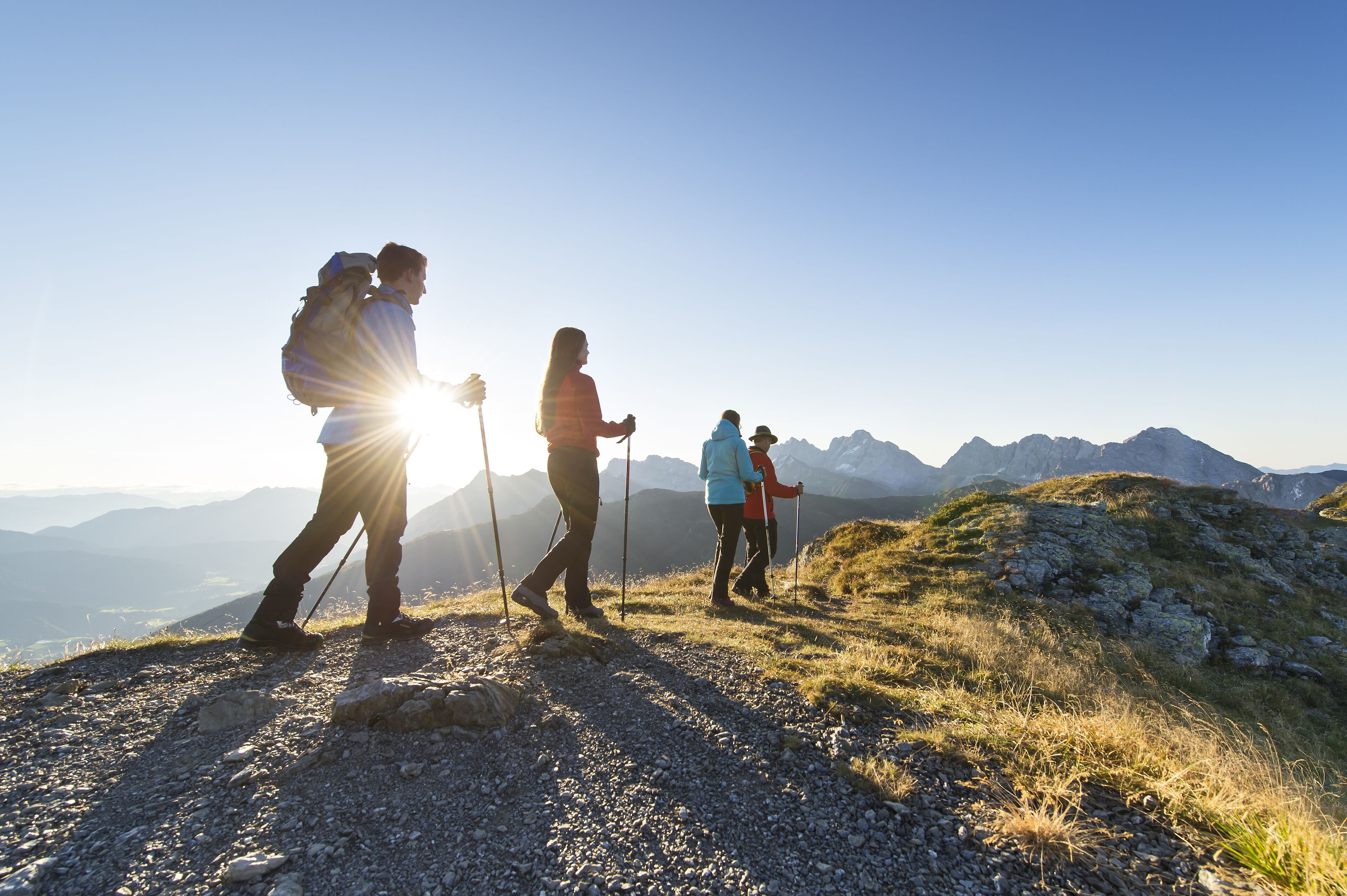 Een groep wandelaars op een bergpad met een heldere lucht en verafgelegen bergen.