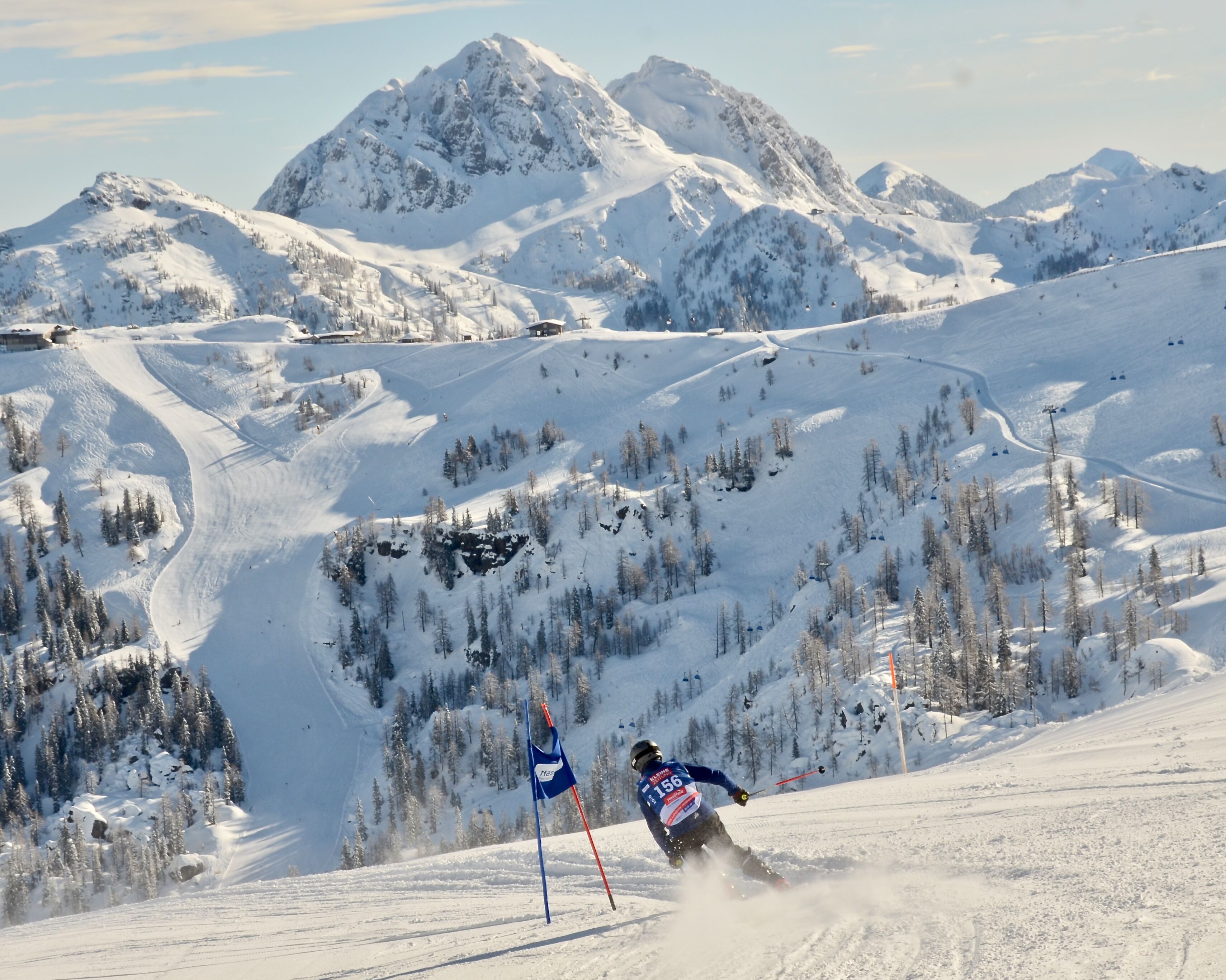 A ski slope with a skier in motion, surrounded by snow-covered mountains and trees.