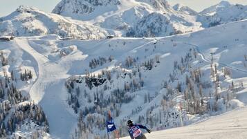 A ski slope with a skier in motion, surrounded by snow-covered mountains and trees.