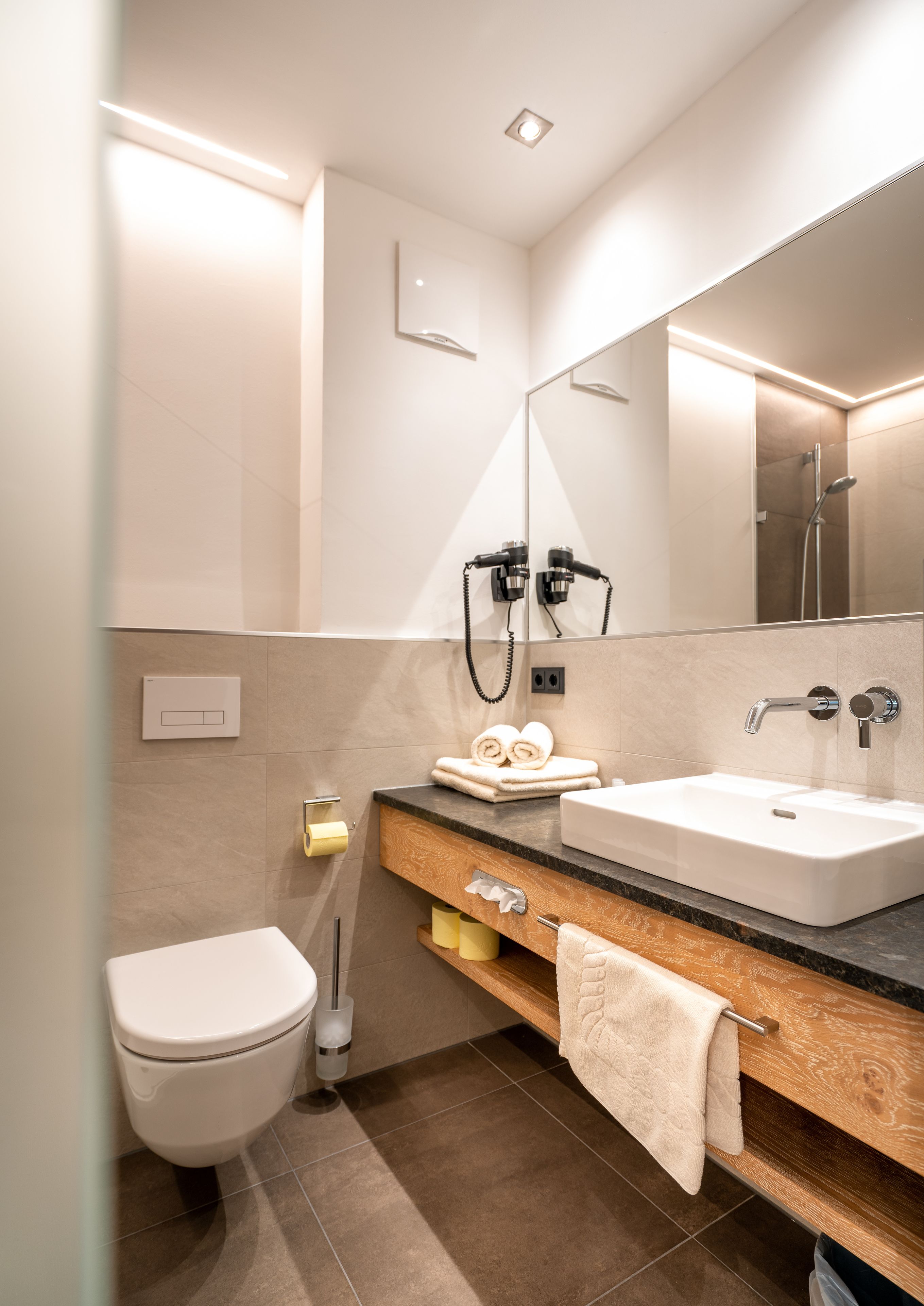Un baño moderno con inodoro blanco, lavamanos con espejo y un perchero para toallas.