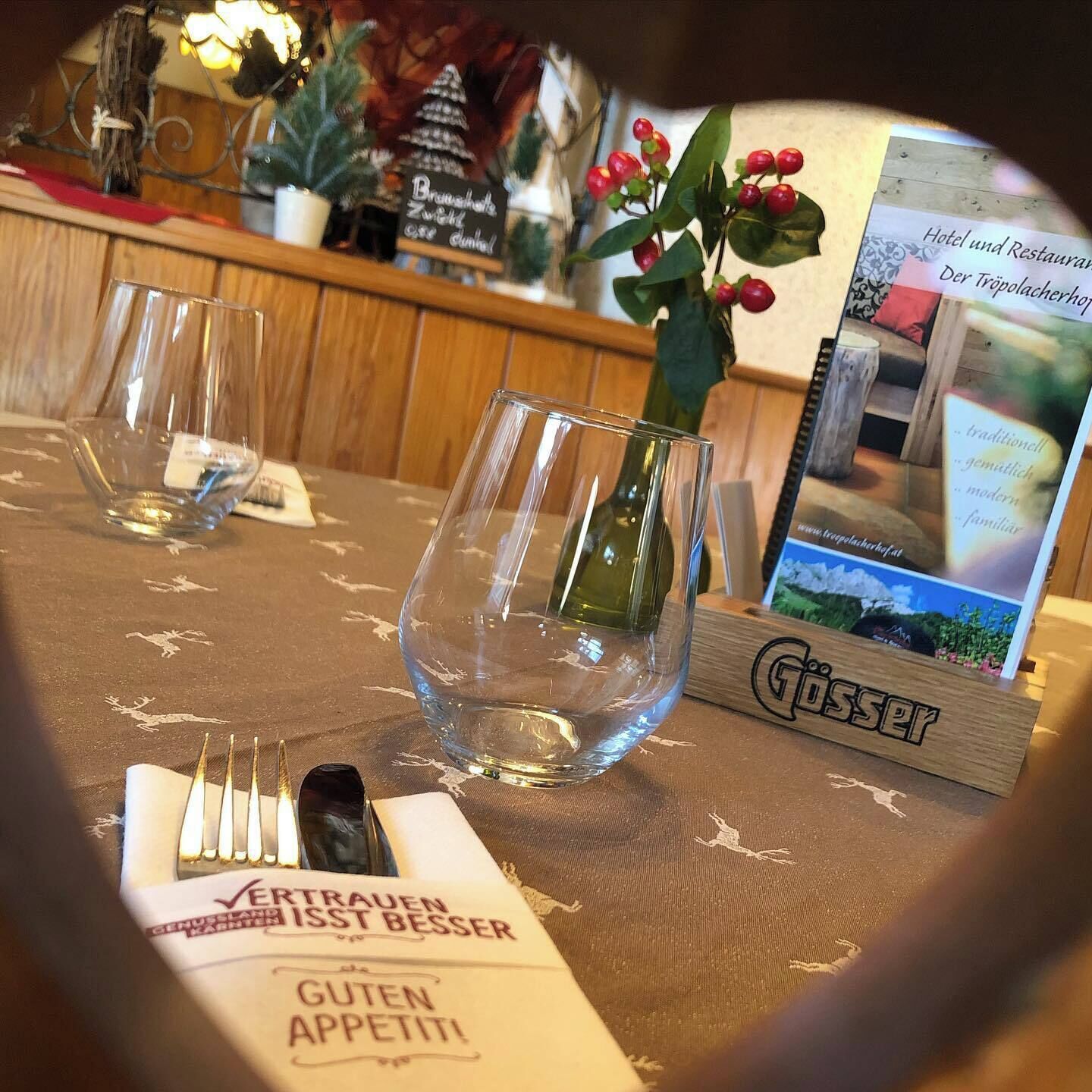 Une table avec des verres à vin vides, une bouteille de vin et un menu sur lequel on peut lire les mots « VERTRAUEN IST BESSER » et « GUTEN APPETIT! ».