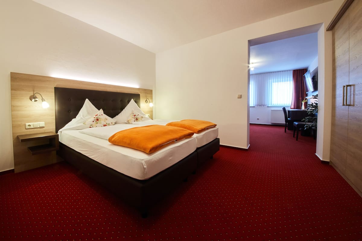 A hotel room with a large bed, two pillows, a nightstand, and a red carpet.