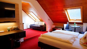 A hotel room with a large bed, a desk with a computer, a flat-screen TV, a sofa, and a small table with a bottle.