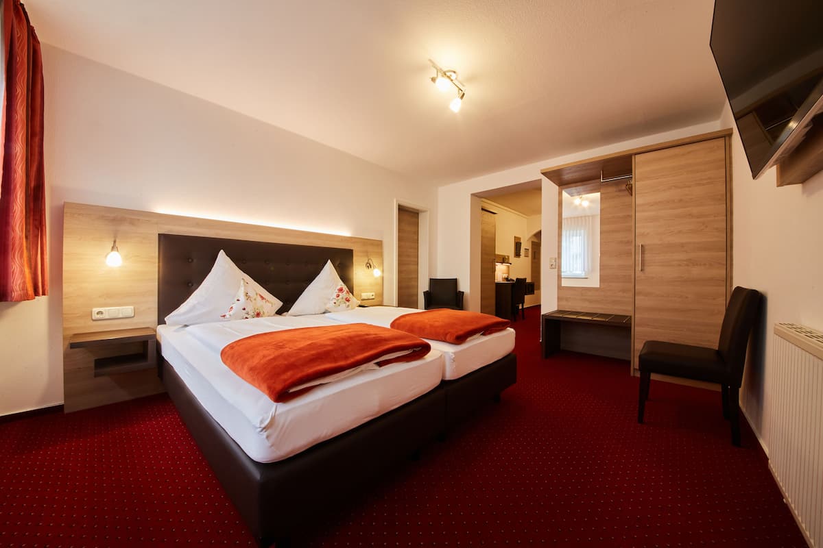 A hotel room with a large bed, a wooden wardrobe, a desk, and a chair.