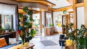 A modern hotel lobby with a sofa, dining table, and potted plants. - Hotel Schoos (Fleringen)