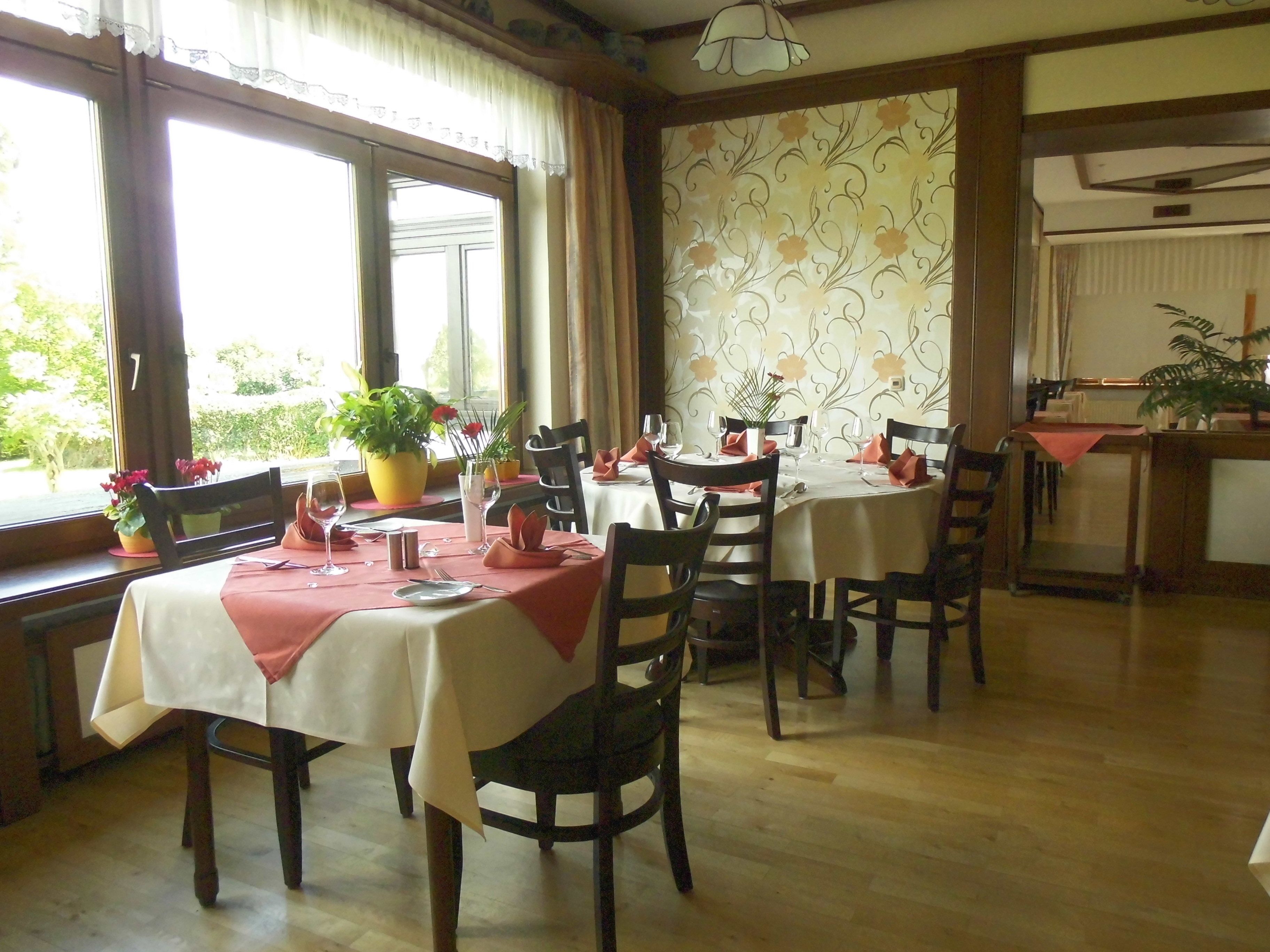 A dining area with tables set for two, featuring white tablecloths and red napkins.